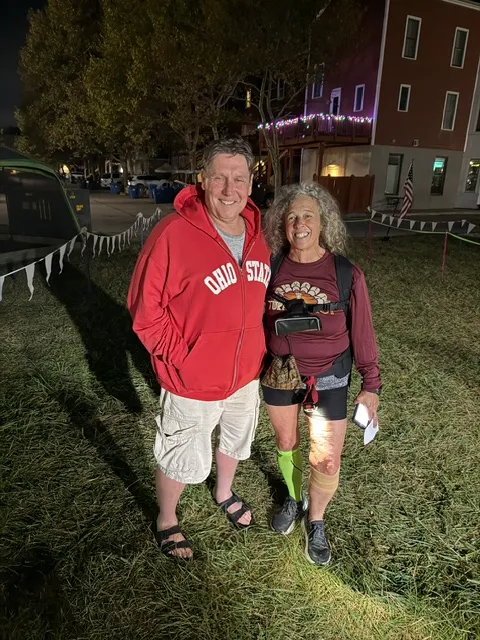 Man in red Ohio State hoodie stands beside smiling woman runner with headlamp, running vest and green compression sock at night