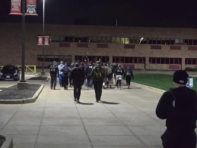 Group of people with backpacks walking away at night along a lit walkway toward a brick high school building