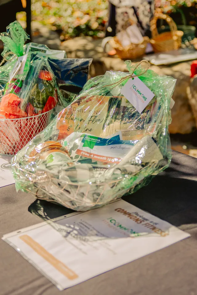 Cellophane-wrapped gift basket with The Commons Fitness Center tag and gift certificate on a table beside a bid sheet