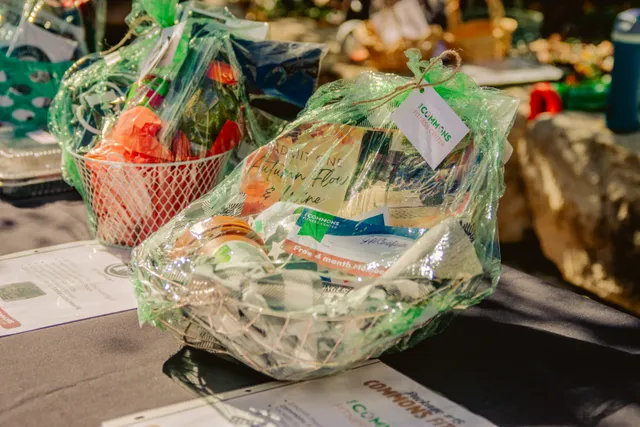 Raffle gift baskets wrapped in green cellophane on a table, one tagged Commons Fitness Center with a gift certificate inside