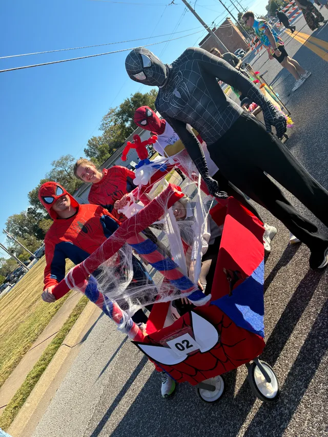 Team in red and black Spider-Man suits with a red Spider-Man themed coffin cart numbered 02, draped in fake webs, on a street