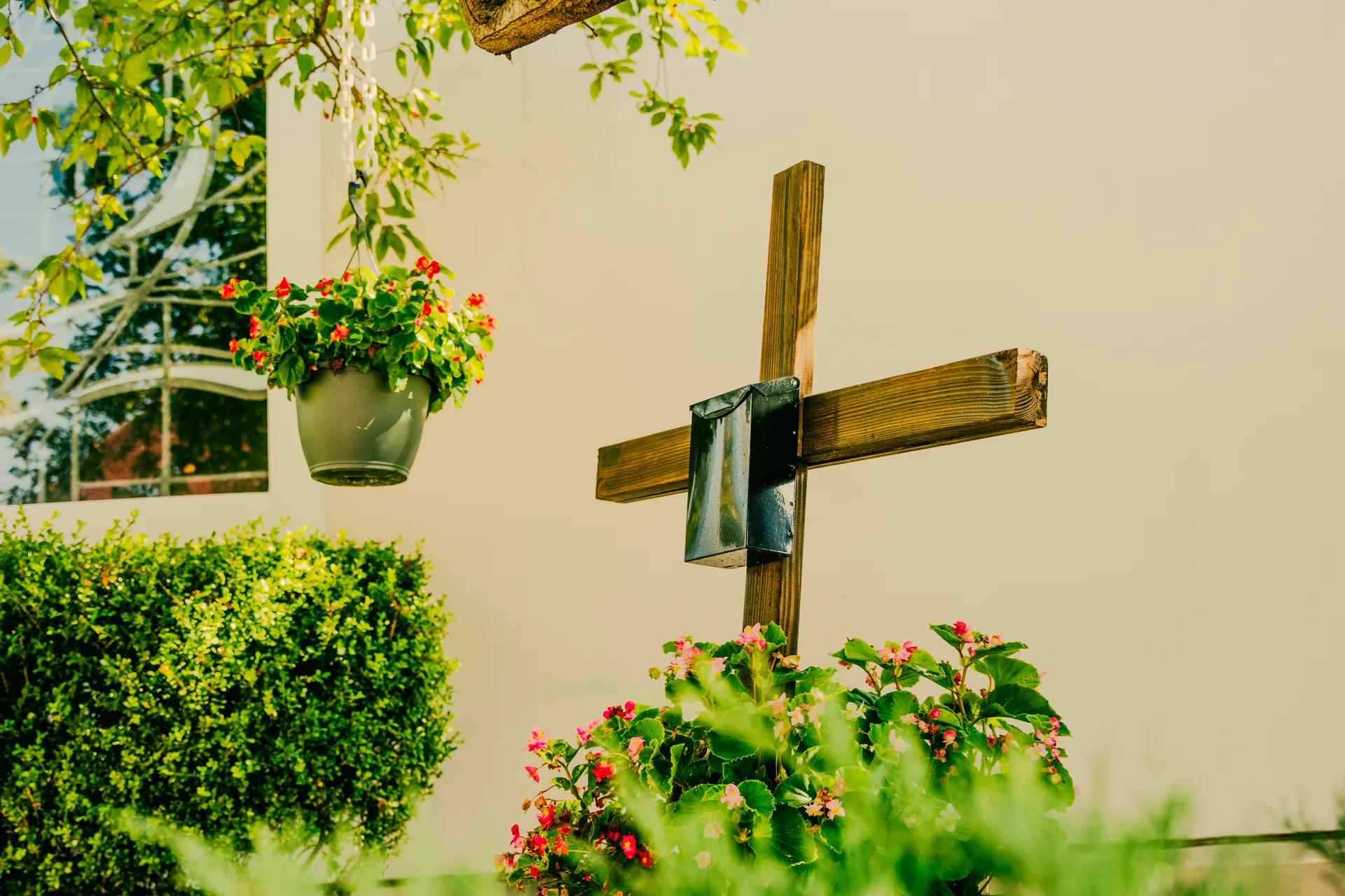 Wooden cross with the prayer request mailbox surrounded by flowers