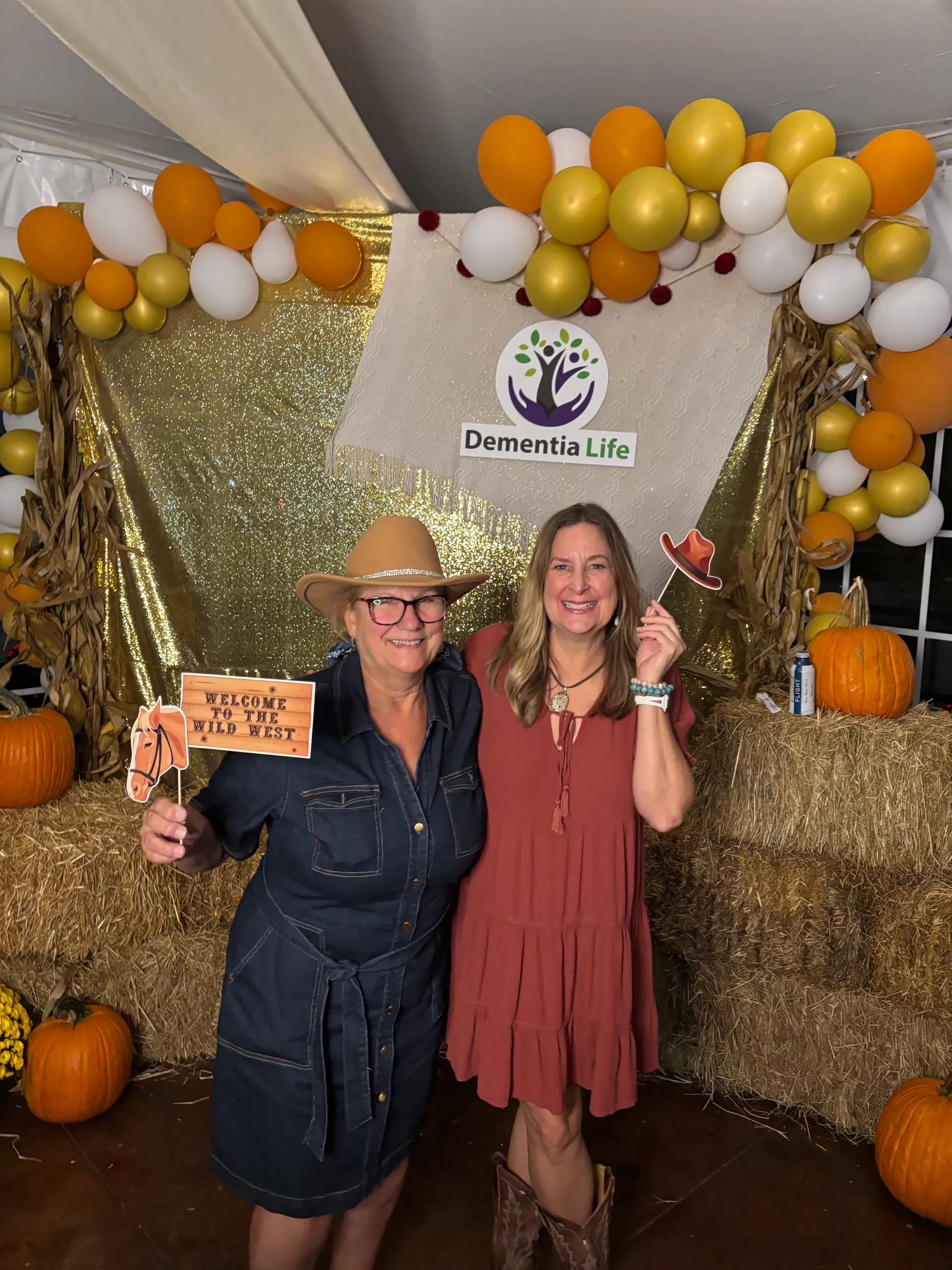 Two smiling guests in western attire pose with props at the Dementia Life Western Whirl photo booth