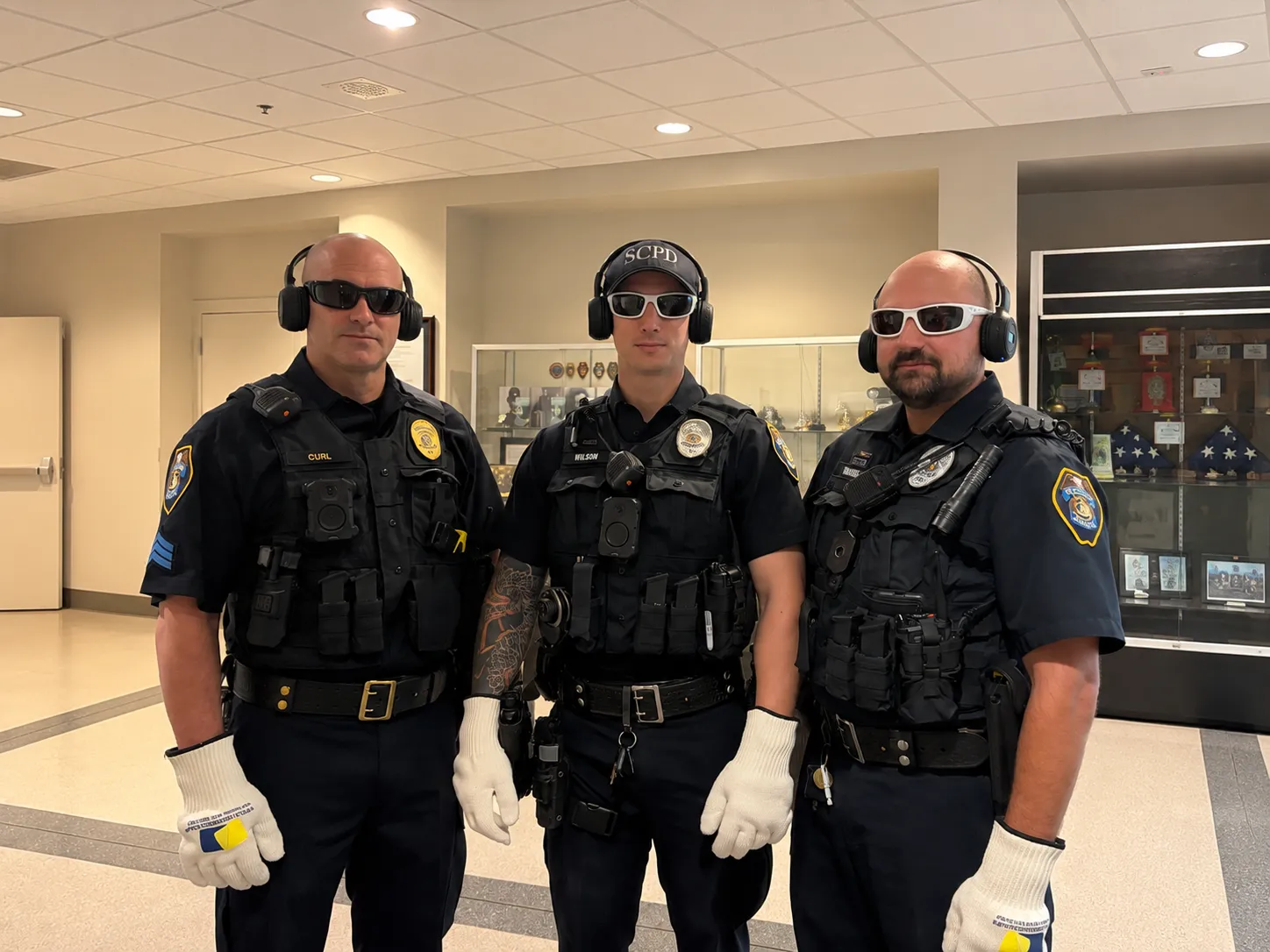 Three police officers wear sensory-simulation headphones, glasses, and gloves during dementia awareness training