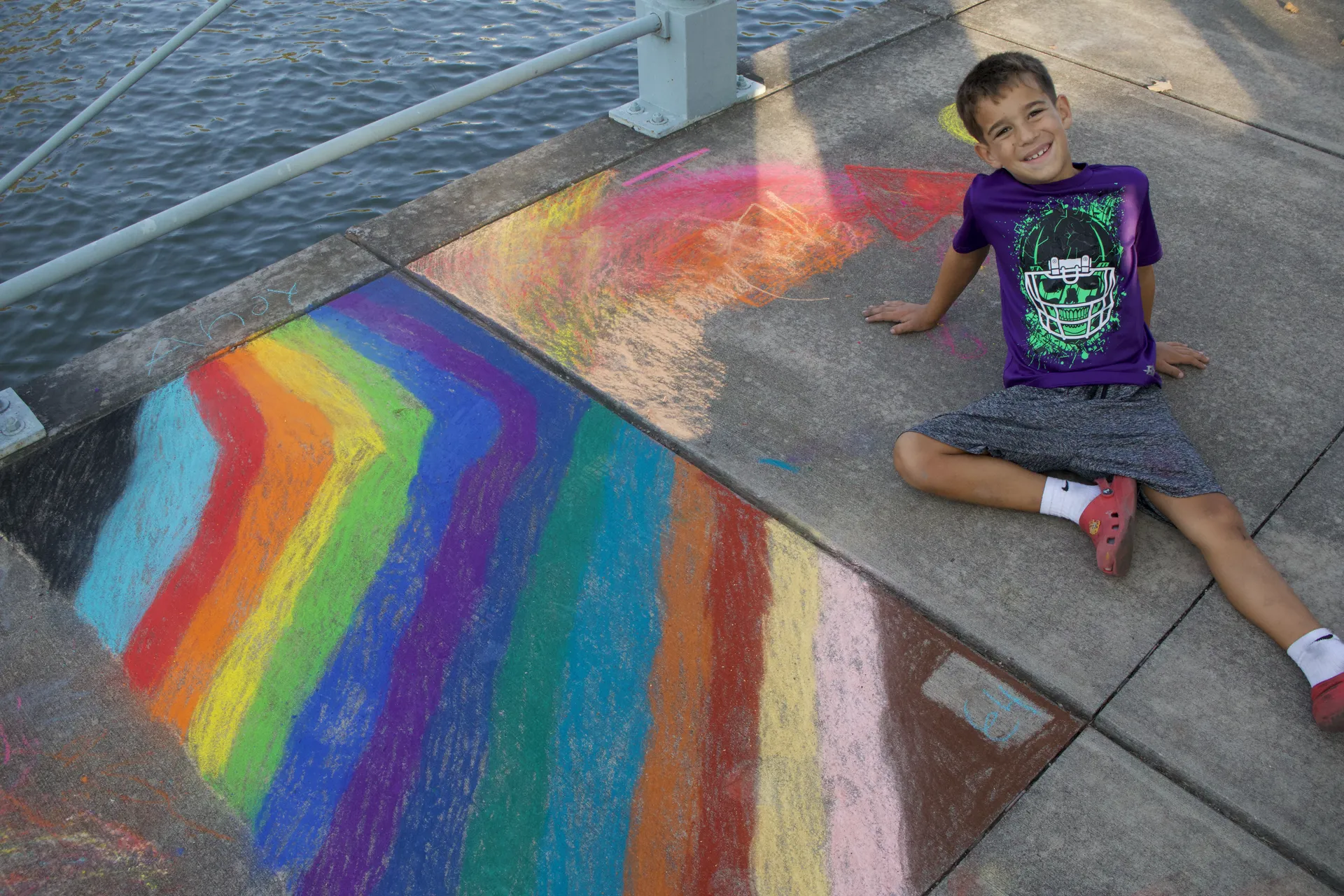 A young artist smiles beside colorful chalk art at Chalk the Walk