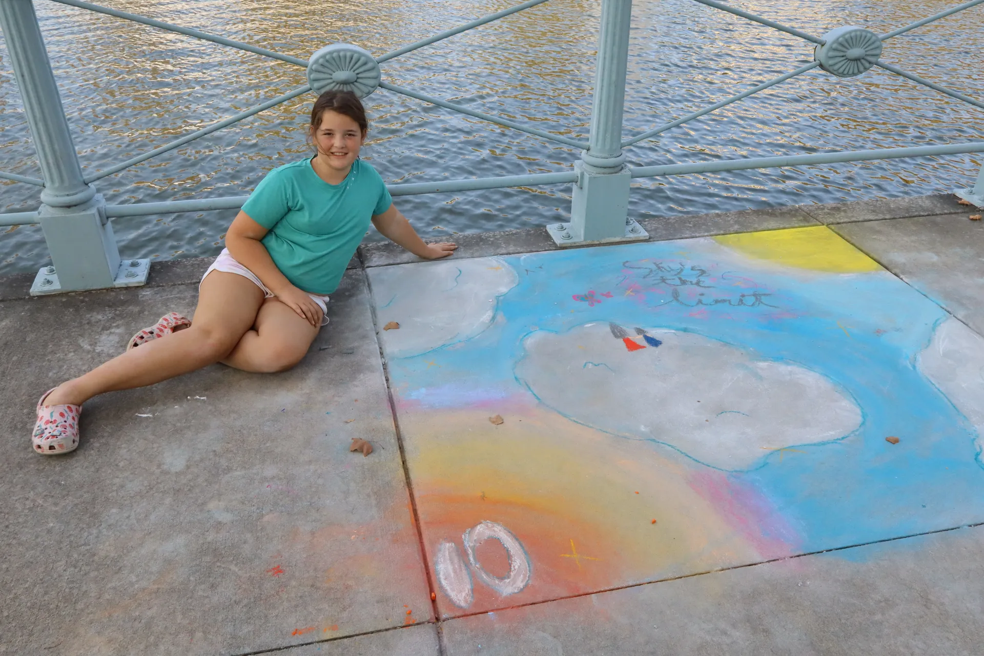 A girl poses with her 'Sky's the Limit' chalk drawing on the sidewalk along the Grand Canal at Chalk the Walk