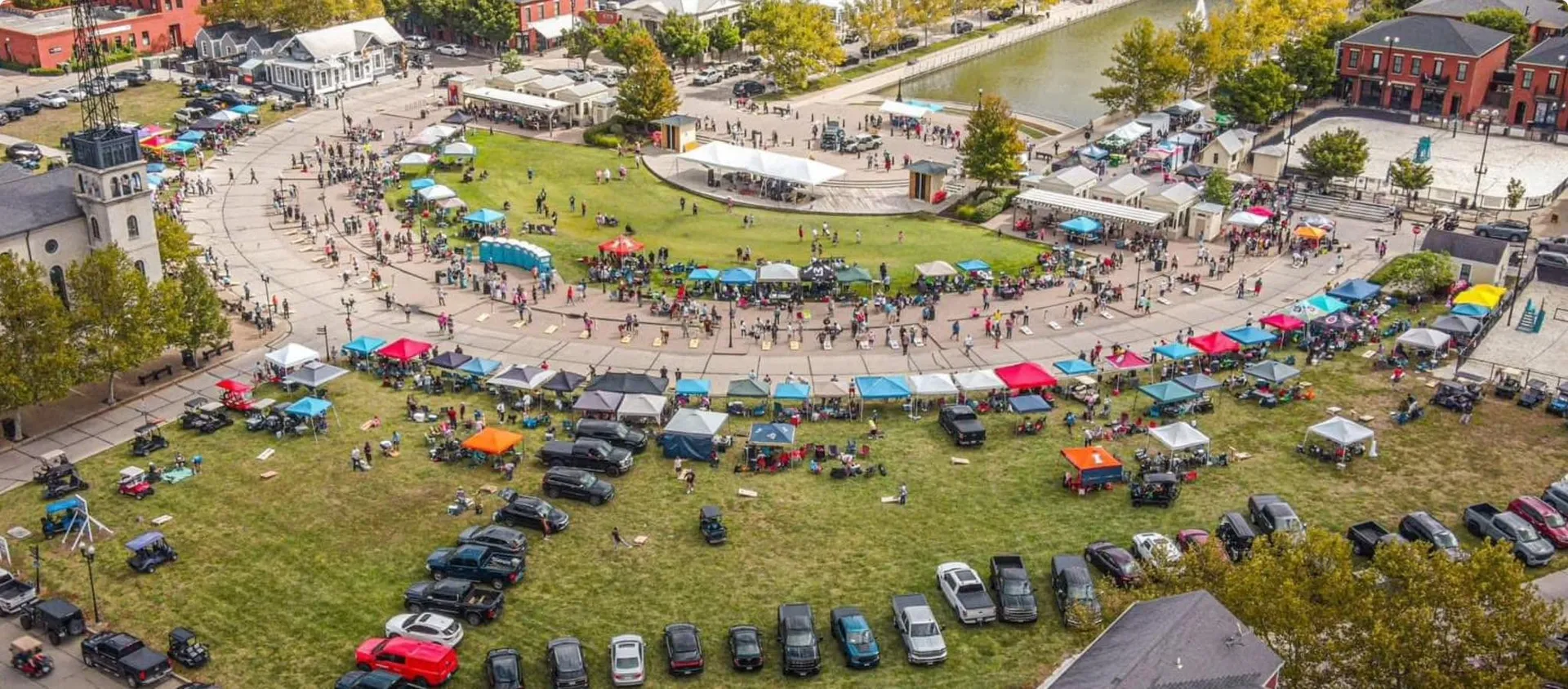 Aerial view of the New Town Throwdown Cornhole Tournament at the New Town Amphitheater, with tents, cornhole boards and crowds circling the lawn