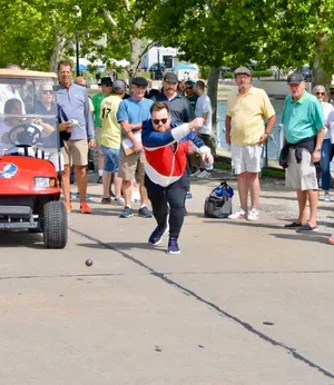 A player hurls the ball along the course as spectators and a golf cart follow the action