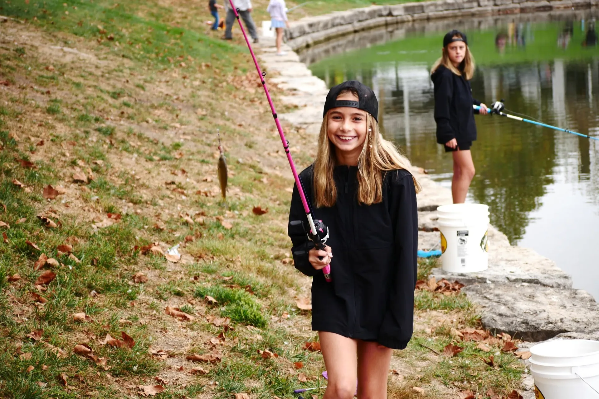 A young angler smiles while holding up her rod with a bluegill on the line