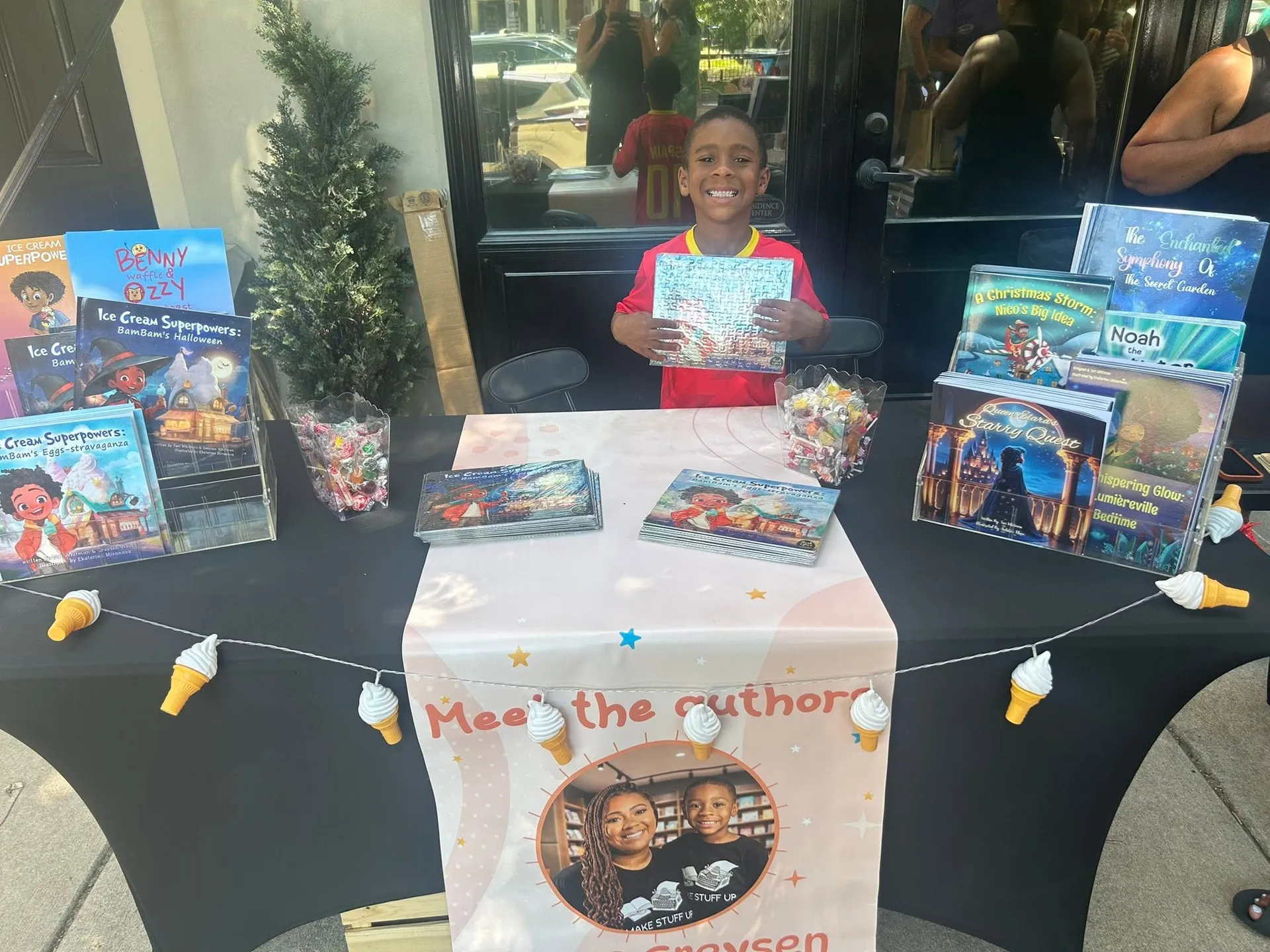 A young author smiles behind a table of his children's books at the Kids Vendor Fair on Rue Royale