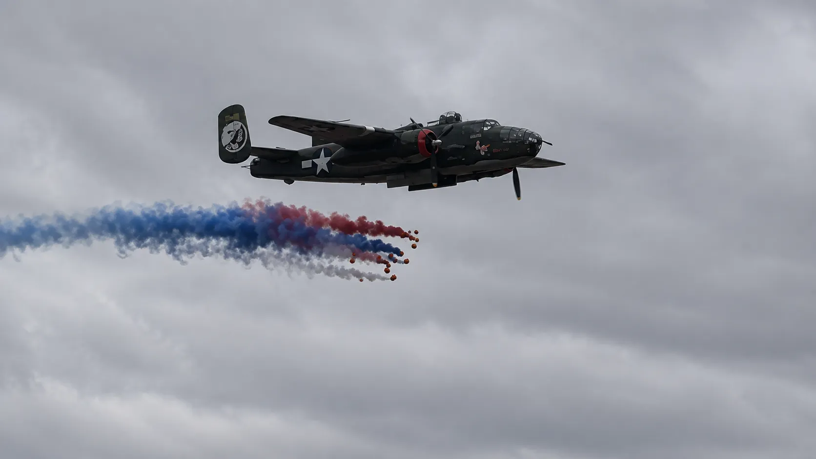 A B-25 bomber releases pumpkins trailing red, white and blue smoke during the Pumpkin Drop
