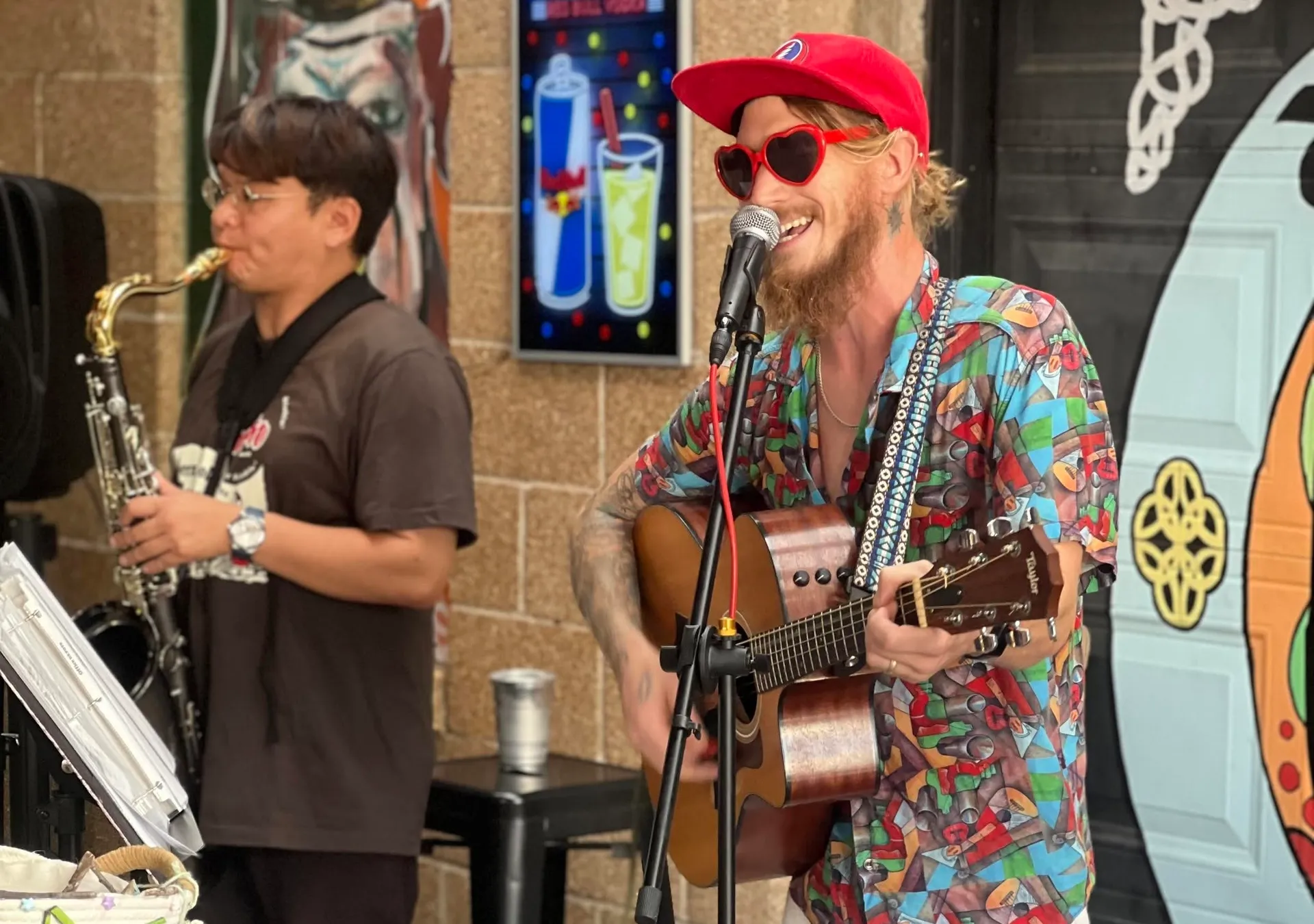 Noah Smith singing and playing guitar in heart-shaped sunglasses alongside a saxophone player