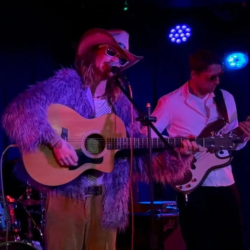Deadly Swift performing on stage in costume with acoustic guitar and bass under purple stage lights