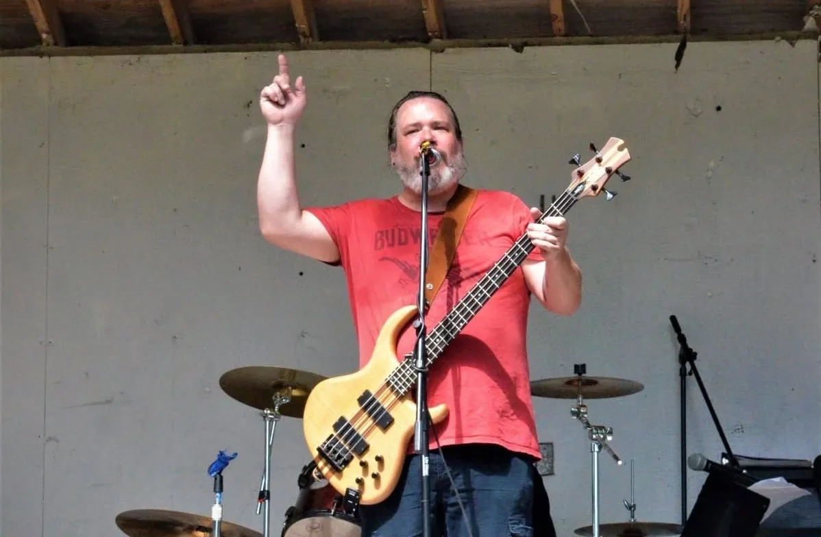Musician performing on stage with a bass guitar, one hand raised
