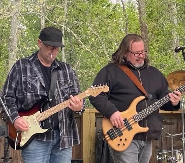 Two musicians playing guitar and bass at an outdoor performance
