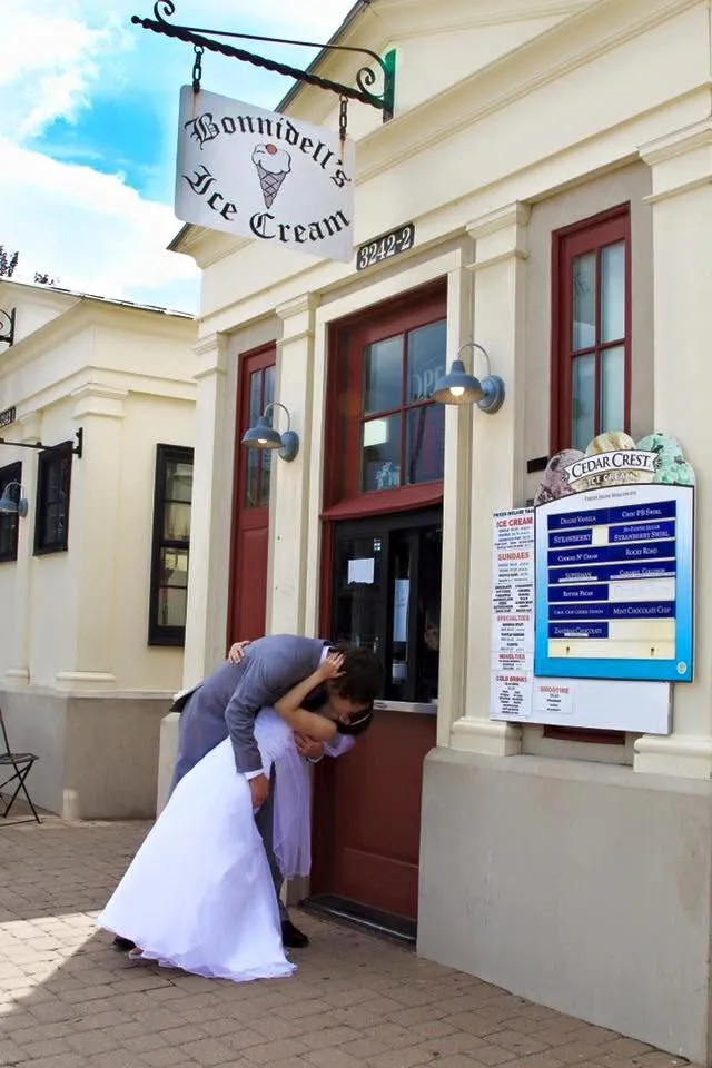 Jessica and Greg share a kiss in wedding attire in front of the Bonnidell's Ice Cream kiosk, where their relationship began.