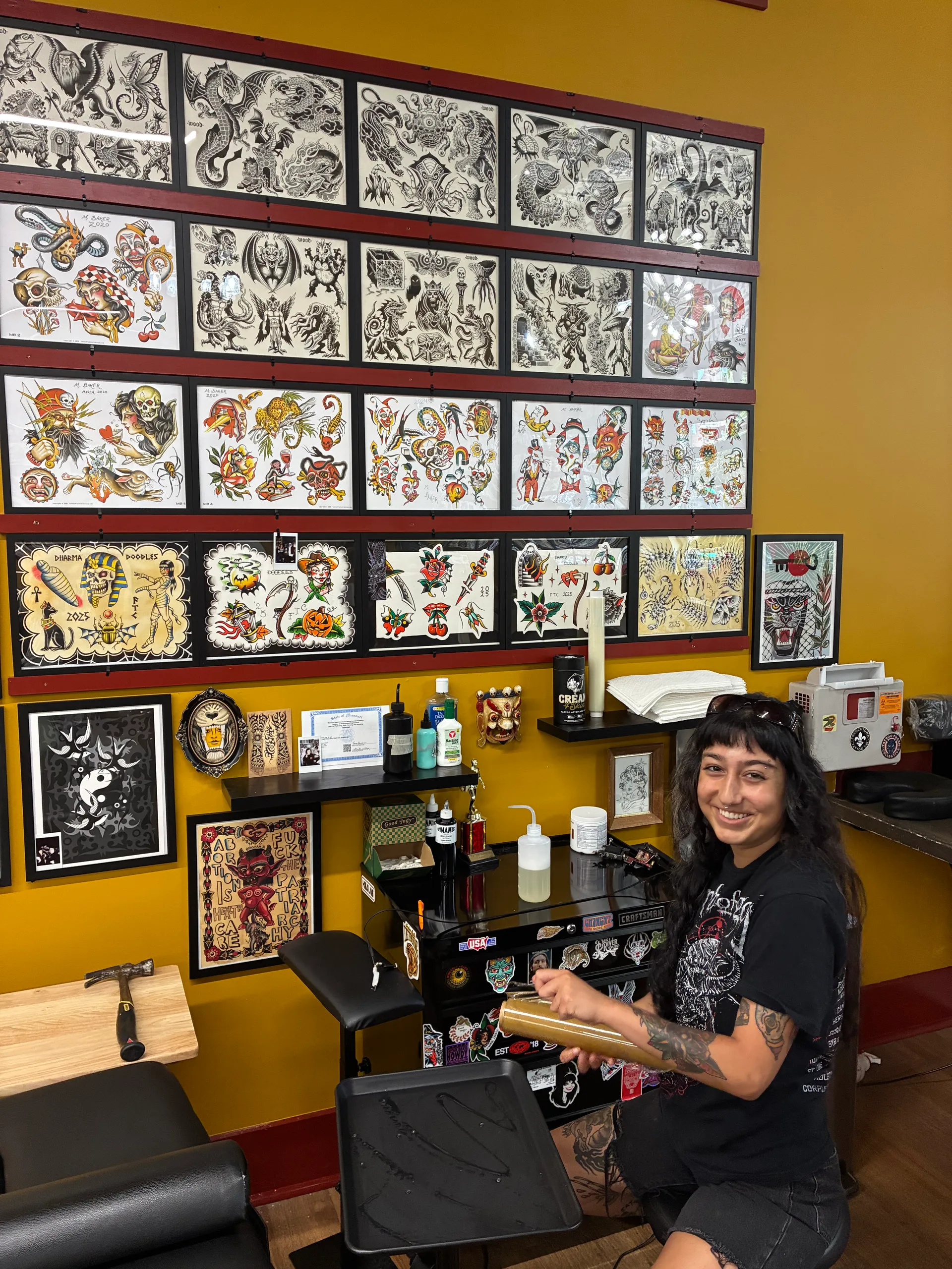 An artist at her station beneath walls of classic tattoo flash at Frenchtown Tattoo Company