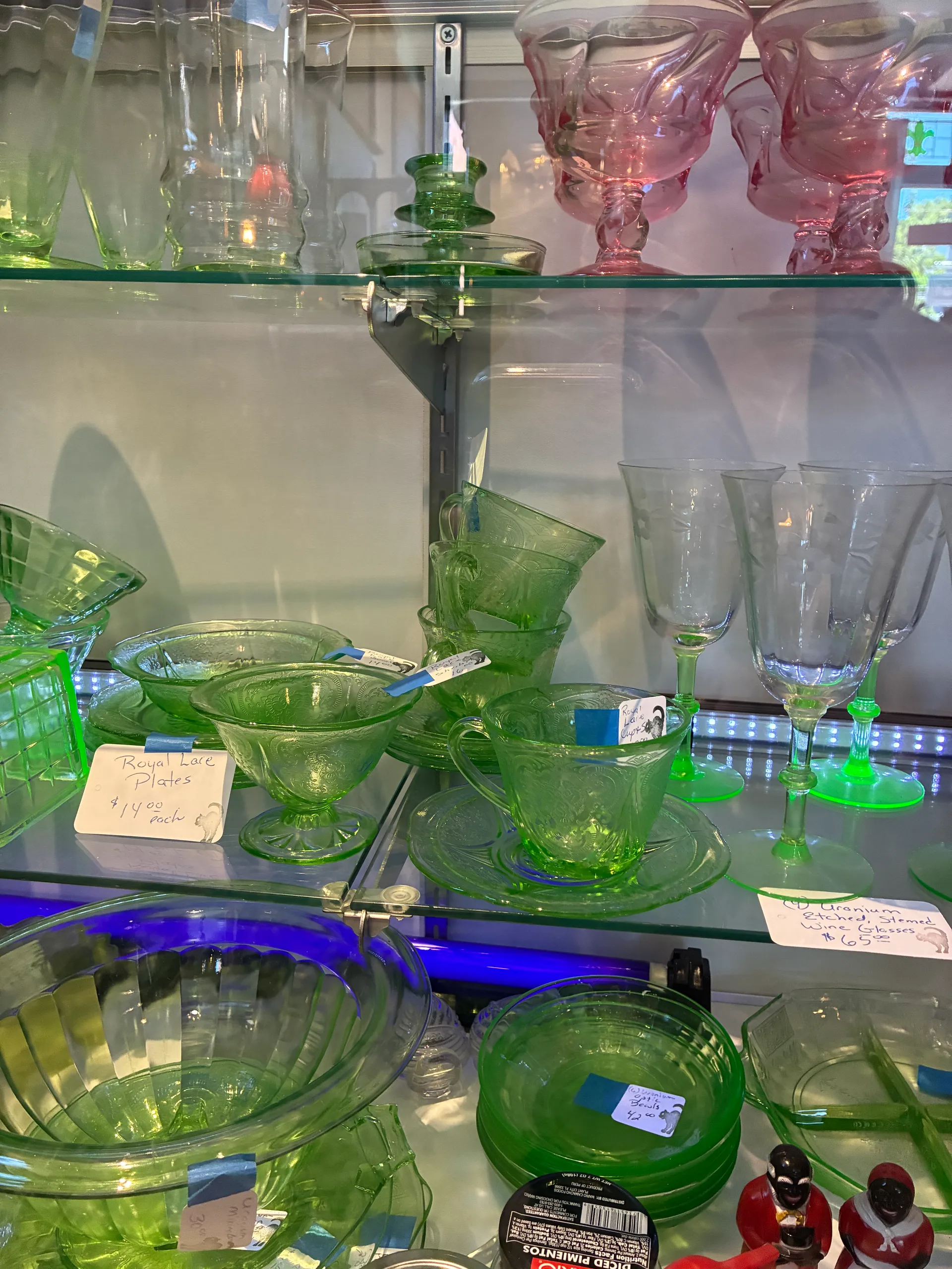 Green uranium and pink depression glass pieces on display shelves at Black Cat Antiques and Such