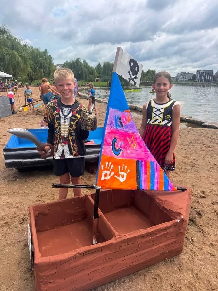 Two kids in pirate costumes with their hand-painted cardboard pirate ship