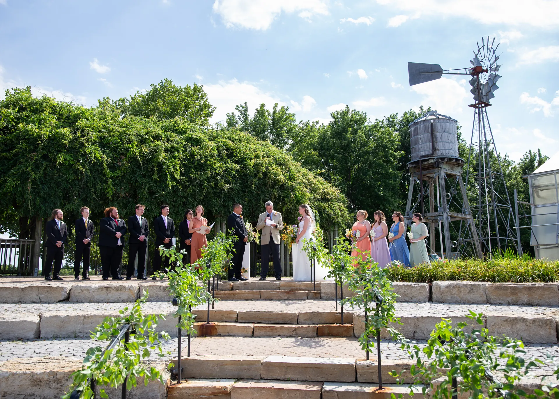 The full wedding party gathered on the stone amphitheater steps surrounded by greenery