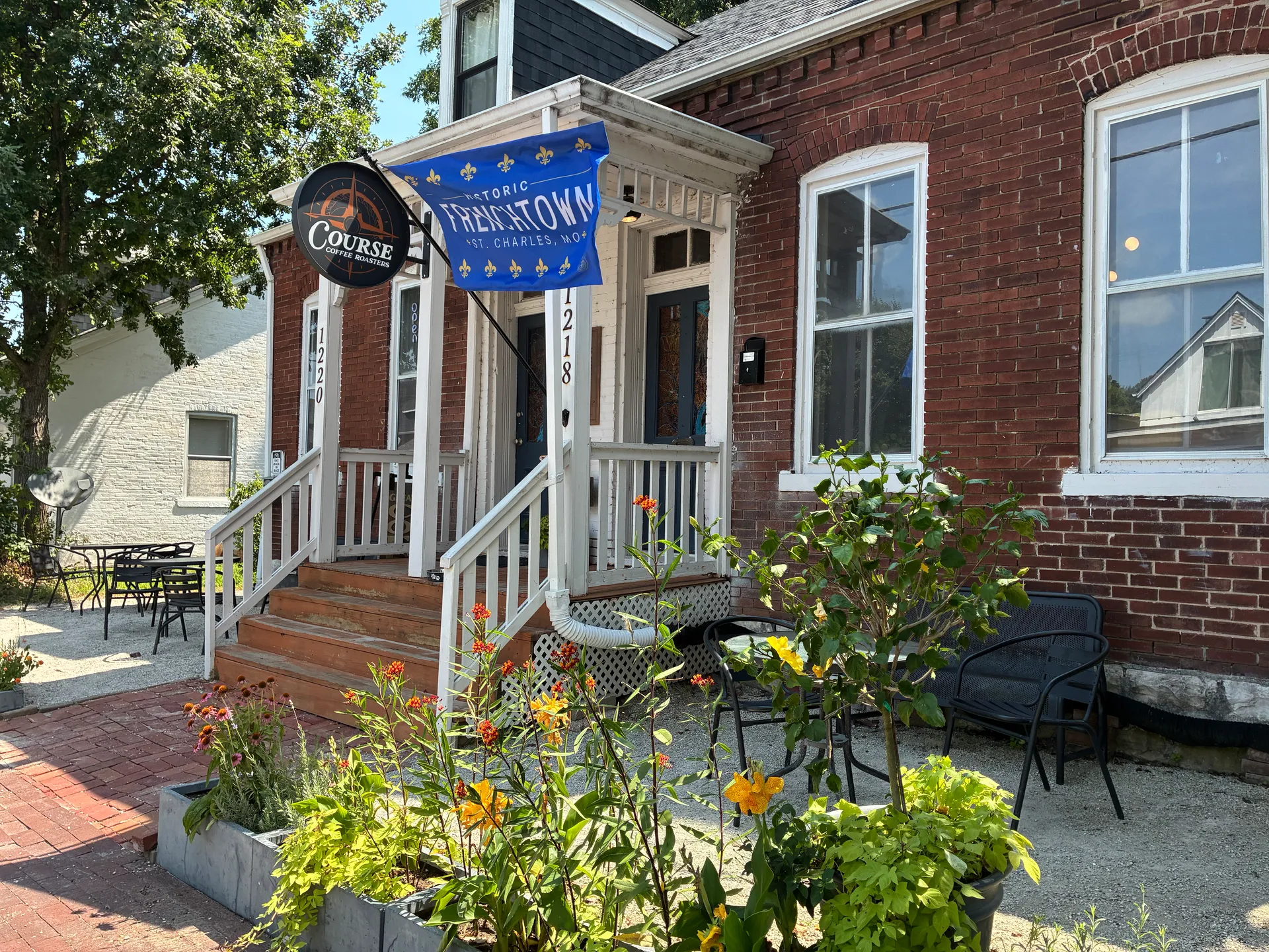 The brick exterior and front porch of Course Coffee Roasters in historic Frenchtown, with its round sign and Frenchtown flag