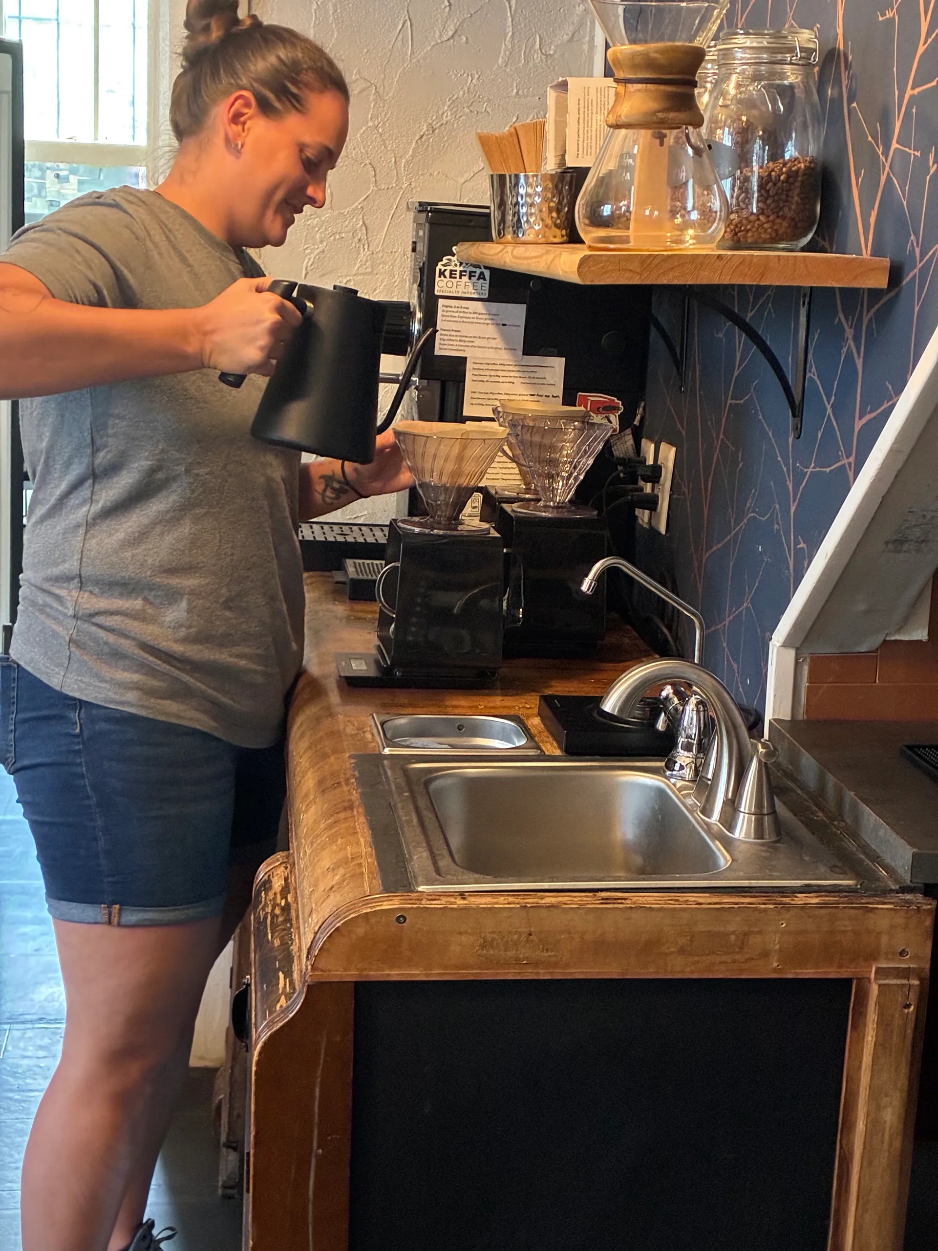 A barista pours hot water from a gooseneck kettle over a pour-over brewer at the coffee bar