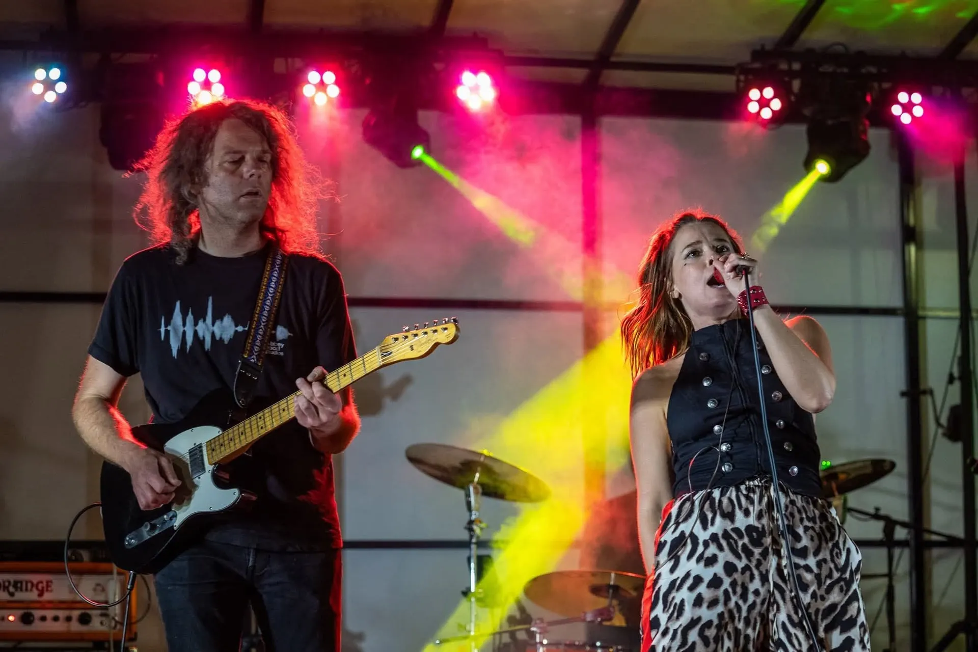 Polly singing on stage with a guitarist under colorful concert lights