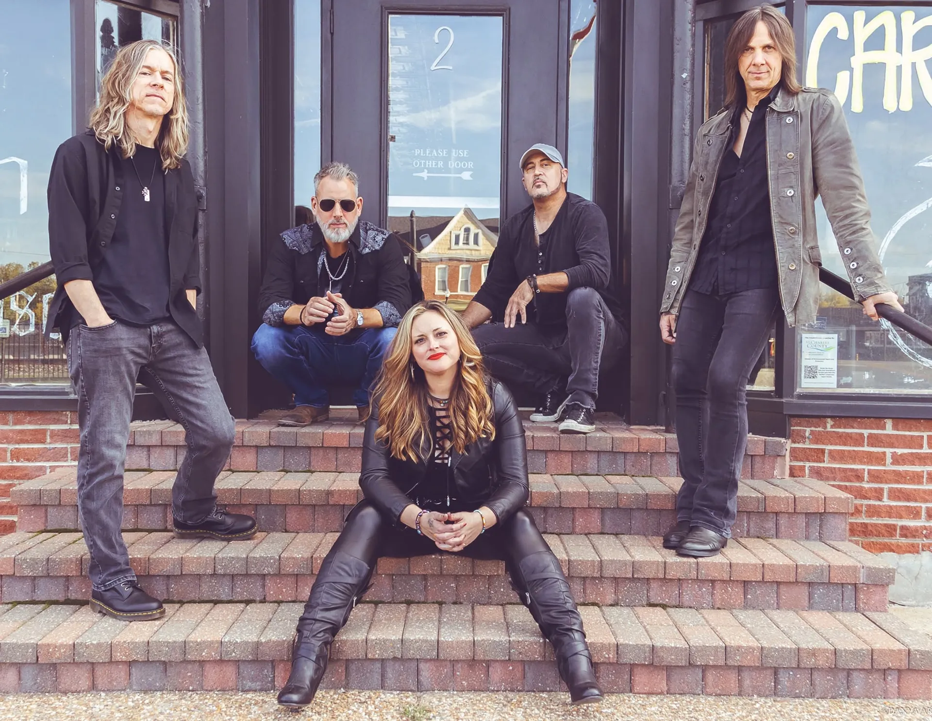 Real Rock Revival band members gathered on brick steps outside a storefront