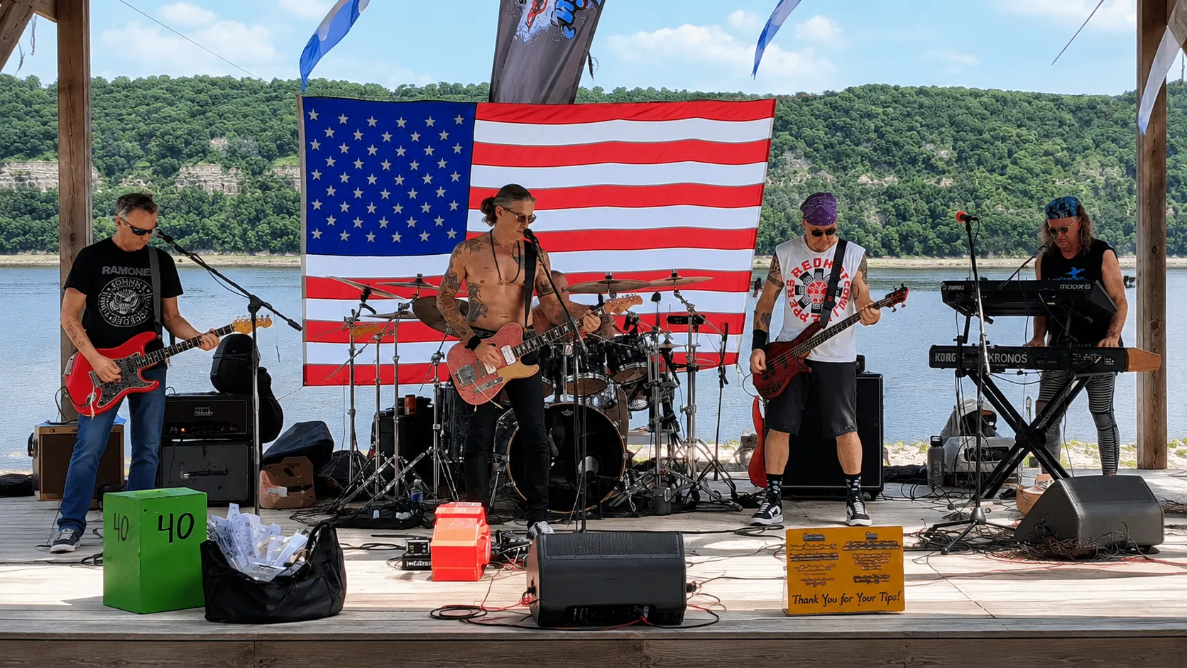 Scarecrow Joe performing on an outdoor riverside stage in front of an American flag